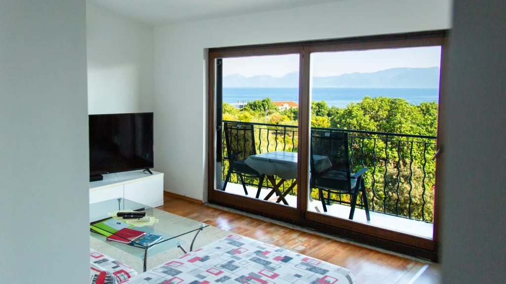 Living room with a television, glass coffee table and sliding doors onto a balcony with sea and mountain views