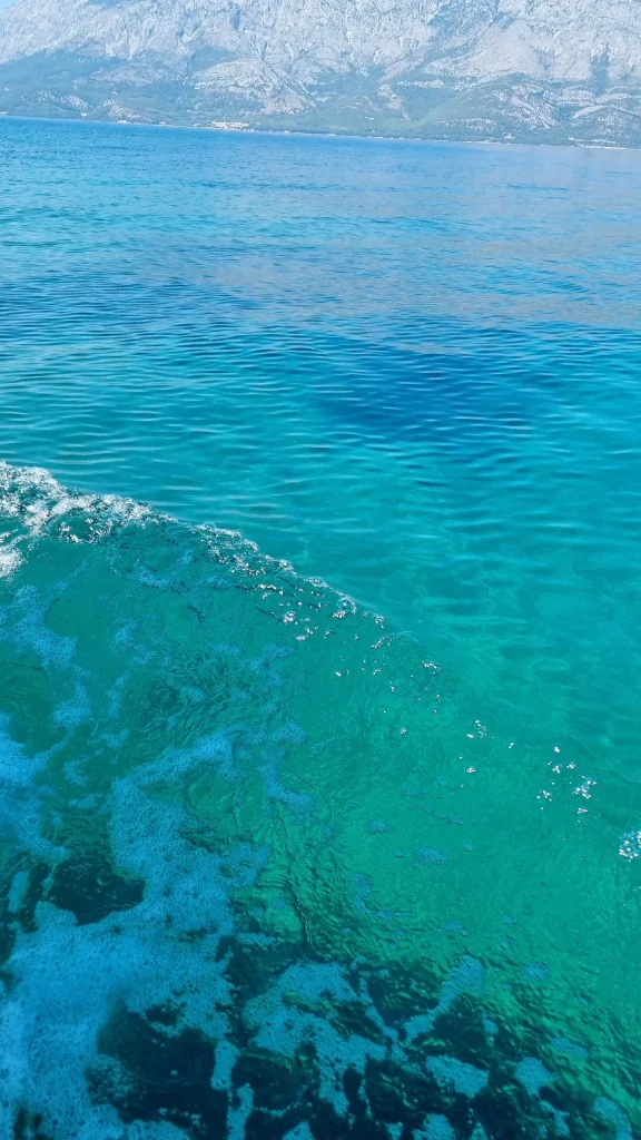 Clear turquoise sea with the seabed showing through, a rocky mountain ridge across the channel