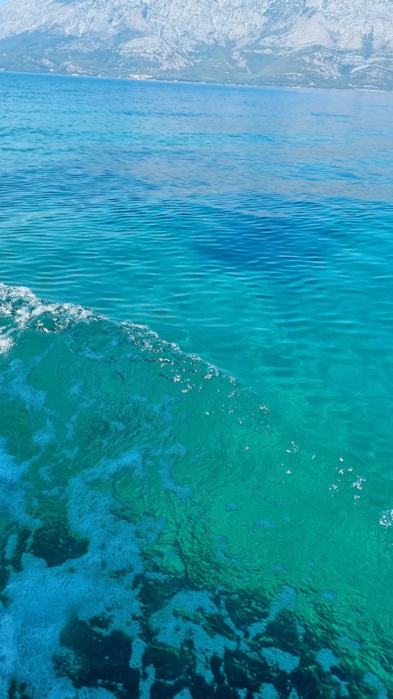 Clear turquoise sea with the seabed showing through, a rocky mountain ridge across the channel