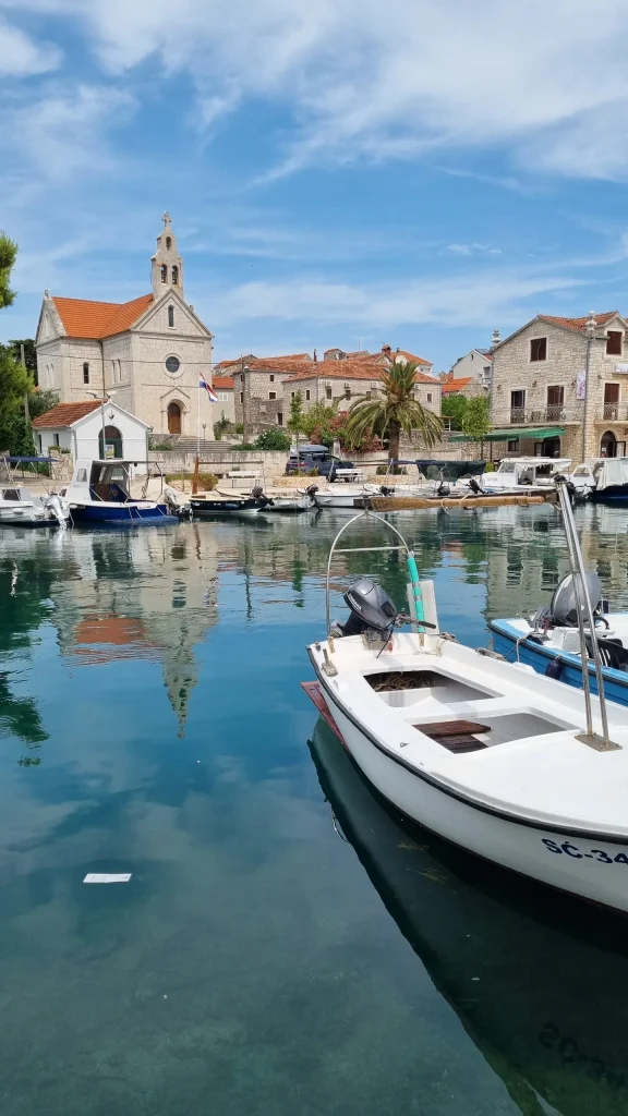 Sućuraj harbour with small boats moored in front of the stone church, houses and a palm tree