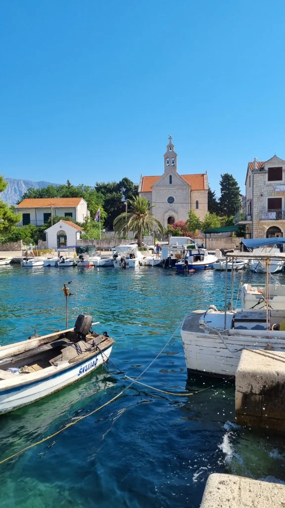 Stone church with a bell tower above Sućuraj harbour, small boats moored in clear water