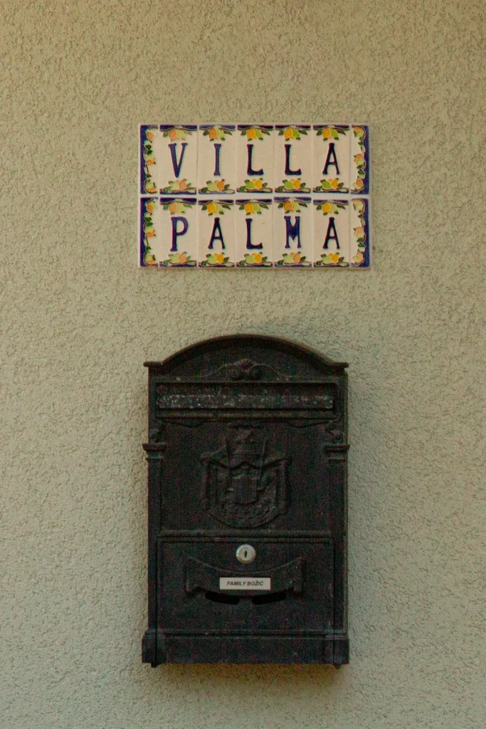 Ceramic tile sign reading Villa Palma with painted lemons, above the dark metal letterbox by the entrance